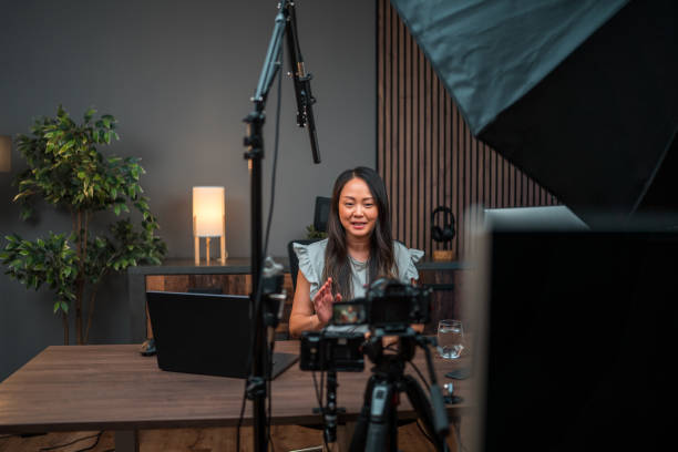 IMG_5052 Showcasing an Asian female content creator in action, this photo captures her dedication. Seated at a table with a desktop PC, she communicates her ideas to the camera. The microphone and strategic lighting equipment enhance the creative atmosphere.